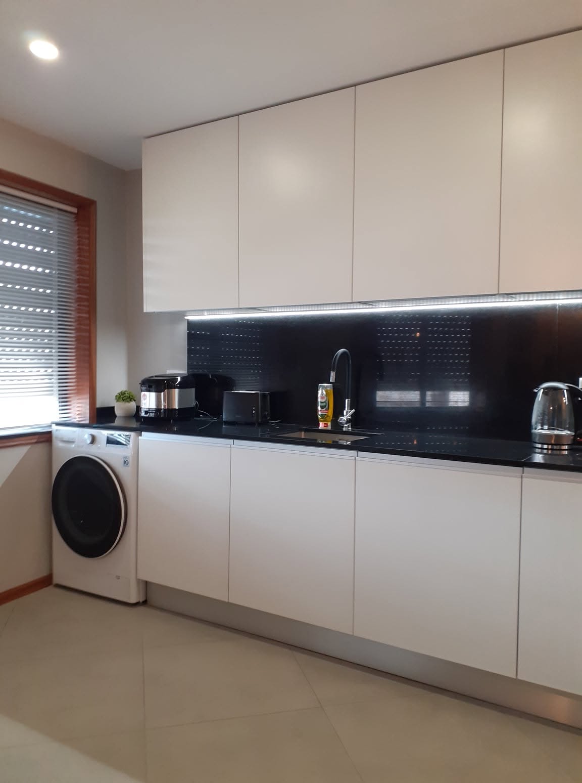 Cozinha remodelada com armários brancos, bancada preta e máquina de lavar roupa integrada