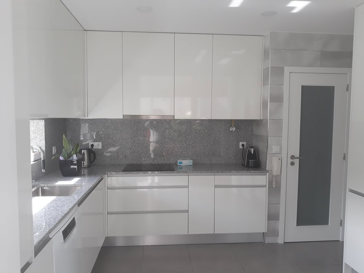 Cozinha remodelada com armários lacados brancos, bancada em granito cinzento e eletrodomésticos integrados