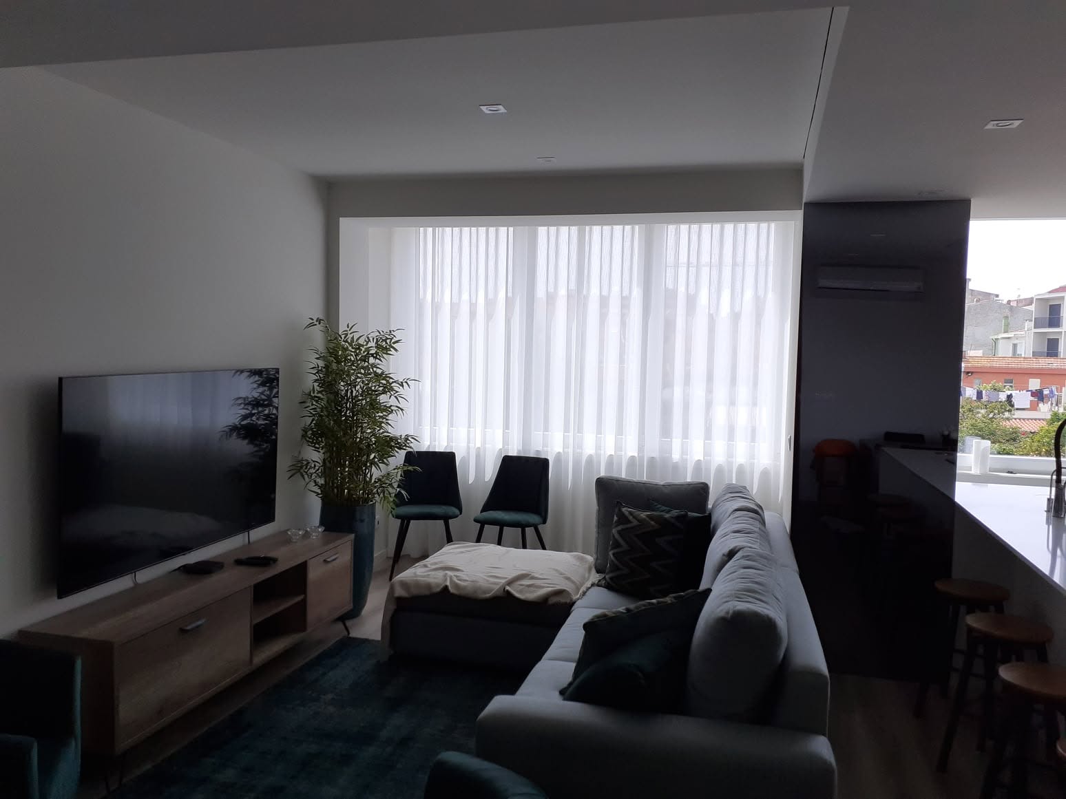 Sala de estar renovada com sofá cinzento, cortinado amplo e ligação à cozinha em open space