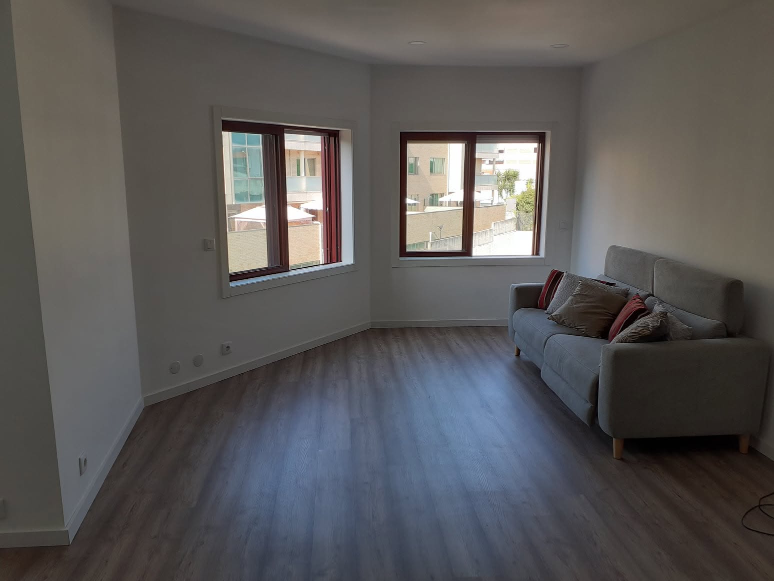 Sala renovada do apartamento T1, com pavimento em madeira e sofá cinzento